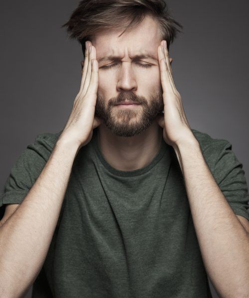 Mann fasst sich an Kopf und verzieht das Gesicht